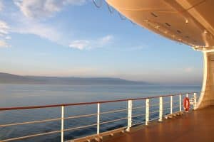 On the open deck of a cruise ship on a calm day, with the coast in the distance.