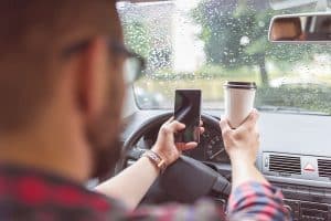 Man using smart phone and having coffee while driving car